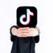 kaukasischer Teenager, der ein Tiktok-Logobild in seinen Händen auf weißem Hintergrund hält. Teenager, die süchtig nach neuen Technologietrends sind. Das Gesicht ist geschlossen.
