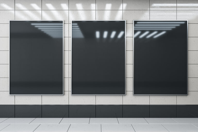 Frontansicht auf drei leere schwarze Werbebildschirme auf heller glänzender Keramikwand mit Lampenreflexion über hellgrauem Boden in leerer unterirdischer Halle.
