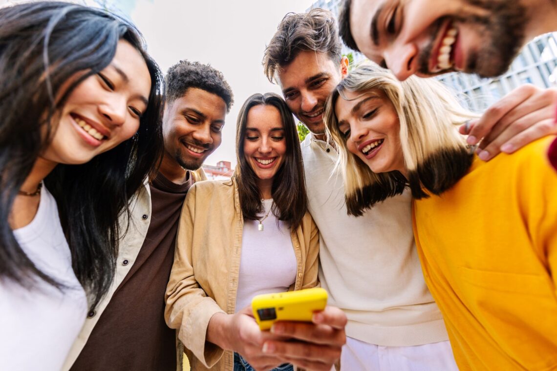 Eine Gruppe junger Freunde schaut gemeinsam auf ein Handy und lächelt, nachdem sie bei Eurojackpot online gewonnen haben.
