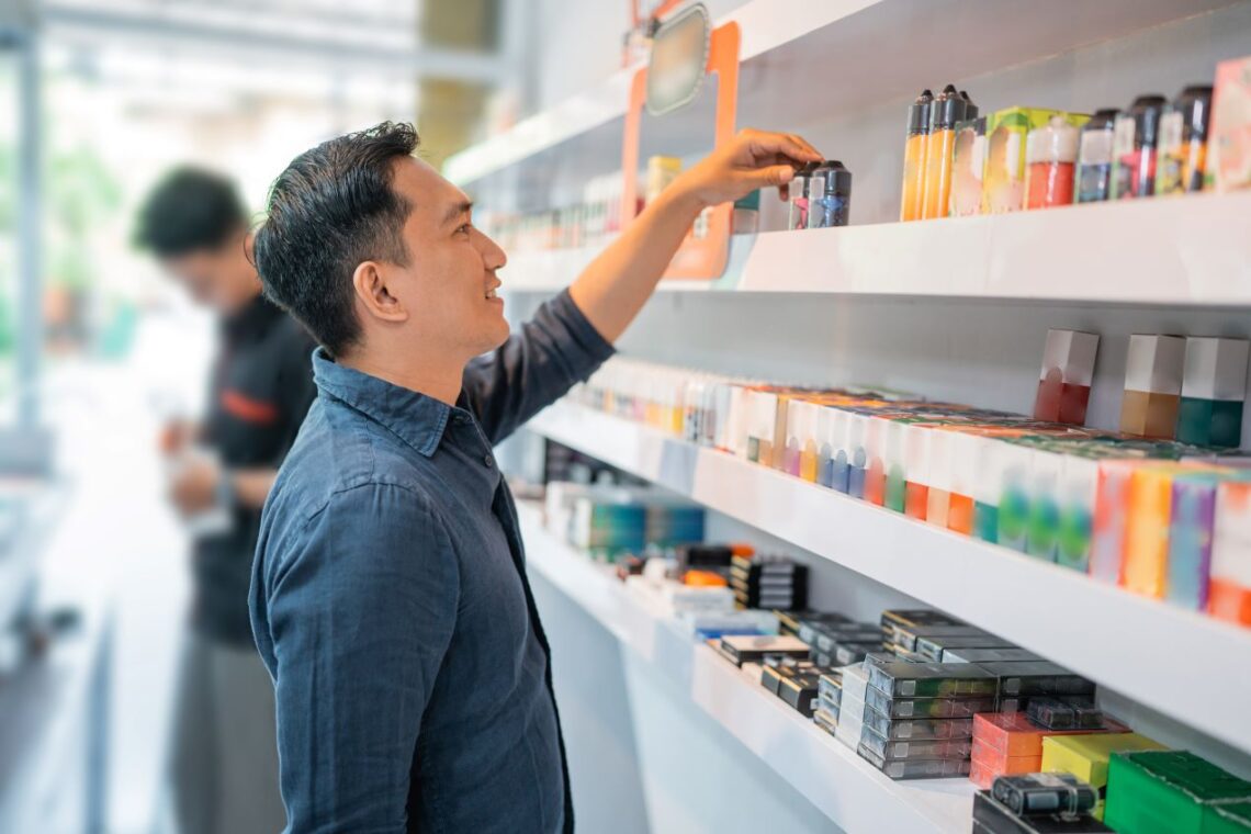 Ein Mann sucht im Vape-Shop nach Elfbar Pods, vor ihm ein Regal mit einer breiten Auswahl an Aromen und Produkten.