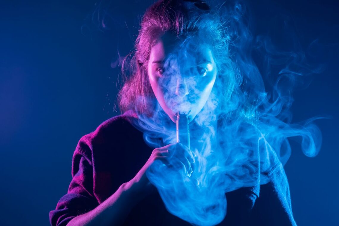 Frau dampft mit E-Zigarette in blauem Licht und testet Elfliq Liquid Geschmack
