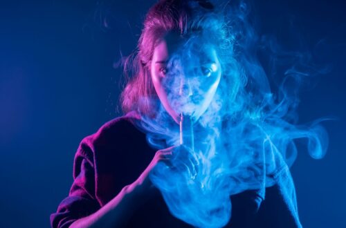 Frau dampft mit E-Zigarette in blauem Licht und testet Elfliq Liquid Geschmack