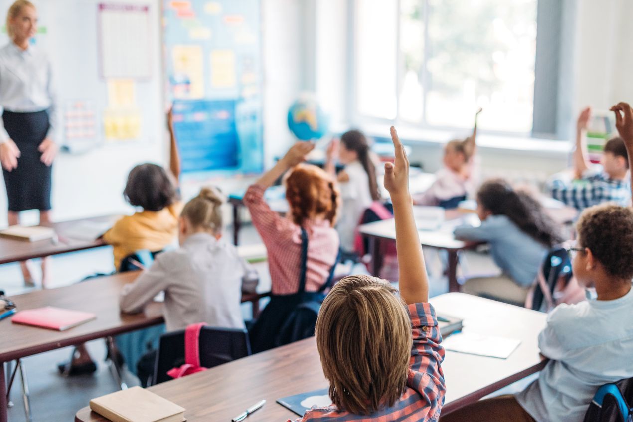 Schuelerinnen und Schueler heben die Hand im Unterricht einer grundschule berlin, moderne Lernumgebung mit Lehrkraft