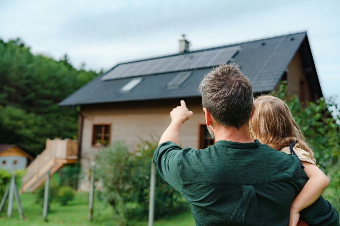 Vater mit Kind zeigt auf Haus mit Solardach – moderne Kombination aus Dachbeschichtung und Photovoltaik