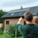 Vater mit Kind zeigt auf Haus mit Solardach – moderne Kombination aus Dachbeschichtung und Photovoltaik